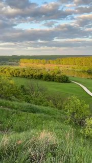 Широкая панорама с холма: зелёные поля, изгиб реки и дальние леса под разрежённым облачным небом