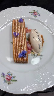 Фарфоровая тарелка с полосатым медовиком, шариком мороженого и синими съедобными цветами, аккуратно сервированная десертная подача.