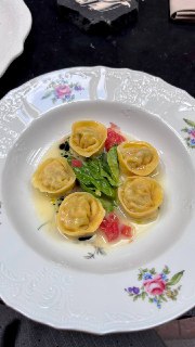 Белая фарфоровая тарелка с равиоли в масляном соусе, зеленью и кусочками томата — минималистичная и аппетитная подача блюда в ресторане.