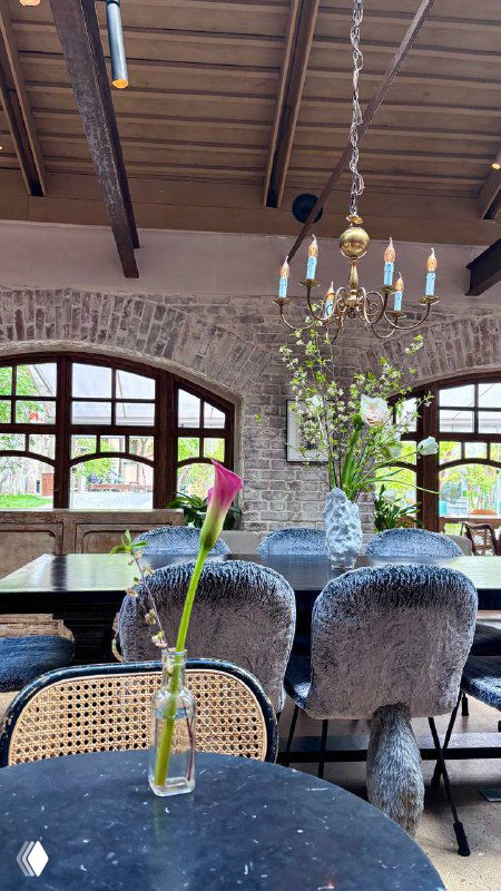 Столовая зона с хрустальной люстрой и арочными окнами, столики у окна с вазочками и винтажным декором под деревянным потолком.