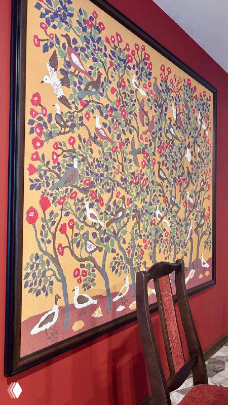 Крупный план большого настенного гобелена с растительным мотивом и декоративными птицами в тёплых тонах, часть обстановки зала.