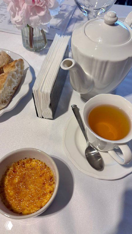 Чайник, чашка с чаем и крем-брюле на белой скатерти рядом с хлебной корзиной — десертная часть ужина на фоне сервировки.