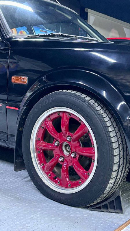 Крупный план колеса и красного литого диска на чёрном кузове ретро-автомобиля, экспозиционная подставка и свет в музее создают атмосферу автоманьячества.