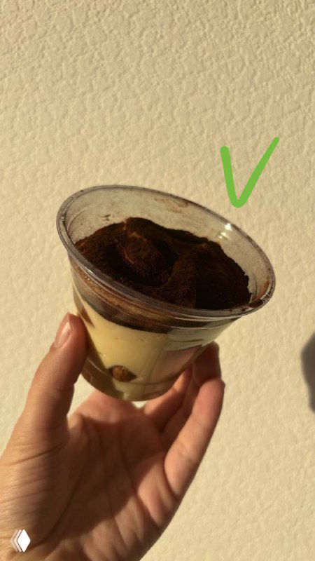 Рука держит пластиковый стаканчик с тирамису на светлом фоне; видны слои крема и какао, пометка галочки о положительном впечатлении.