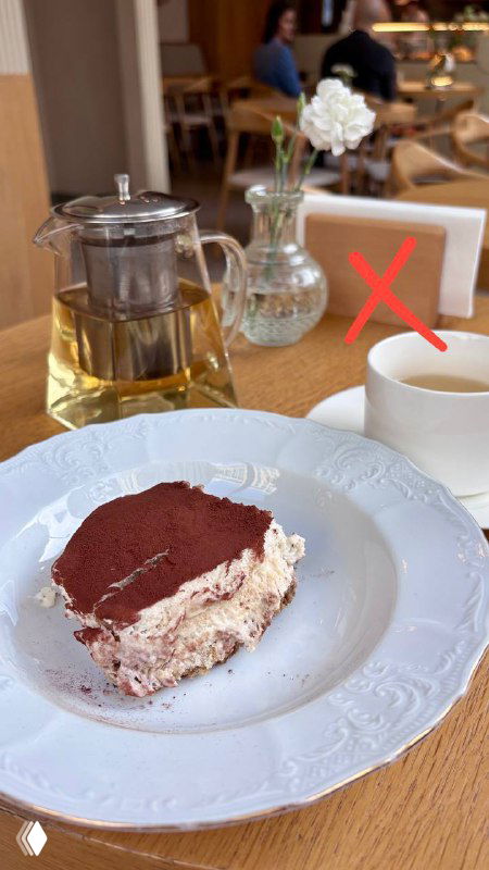 Кусок тирамису на тарелке в кафе рядом с чайником и чашкой; на кадре красный крест, обозначающий неудачную версию десерта.