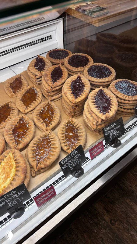 Острые кадры витрины с разными калитками и пирогами в прилавке пекарни; видны формы изделий и ценники у каждой серии печений.