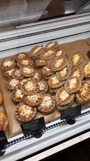 Поднос в витрине с аккуратно выложенными калитками, некоторые украшены белой посыпкой или кремом, общий вид выпечки
