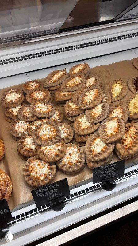 Холодная витрина с маленькими калитками разной начинки: творог, картошка и другие варианты аккуратно уложены в ряд на подносе.