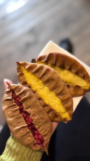 Крупный план двух калиток в руках, видно цветную начинку и аккуратно защипанный край теста, композиция в руке снимавшего