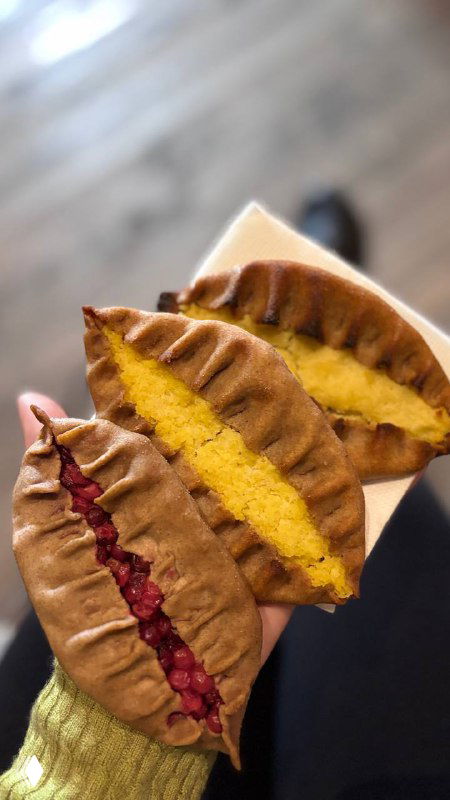 Разрезанные калитки с разными начинками — тёмная ягодная и светлая тыквенно-картофельная; руки держат кусочки на фоне деревянного стола.