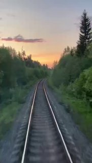 Вертикальное видео из вагона: рельсы уходят в перспективу, закат над лесом и озером, тихая романтичная атмосфера.
