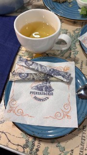Чашка чая на подносе с фирменной салфеткой «Рускеальский экспресс» и пакетиками сахара, сервировка в поезде.