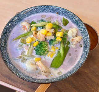 Миска фиолетового рамена с кукурузой, брокколи и зелёными овощами; отчётливо виден необычный фиолетовый бульон и текстура ингредиентов.