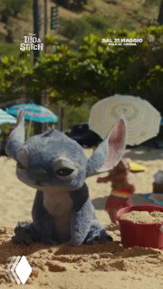 Игрушечный Ститч, оставленный в песке на пляже: фигурка в песочном окружении, зонтики и ведёрко на заднем плане, кадр из трейлера или тизера.