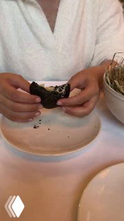 Гости разрывают чёрный пирожок, видно сырную тянущуюся начинку; интерьер и белая скатерть на столе — фото из обзора в Christian, Москва