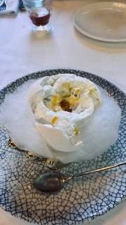 Десерт в тарелке с хлопковой сахарной ватой и кремовой структурой, украшенный соусом и поданный в изящной посуде на столе.
