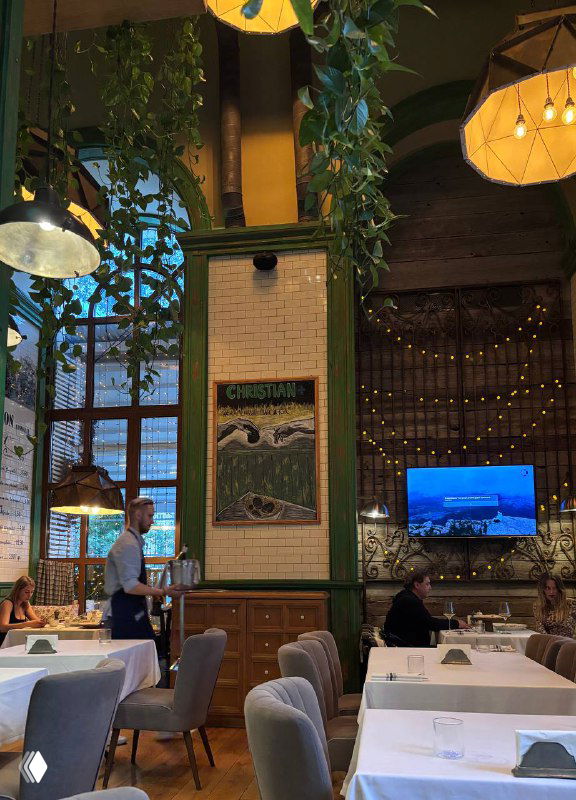 Интерьер ресторана Christian: высокий зал с зелёными колоннами, столами и декоративными элементами, вид на посадочные места и атмосферу заведения в Москве