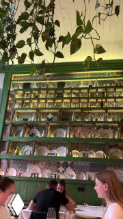 Высокая стеллажная полка с посудой и растениями, посетители у столов внизу — витрина интерьерных решений ресторана Christian в Москве на Кутузовском проспекте