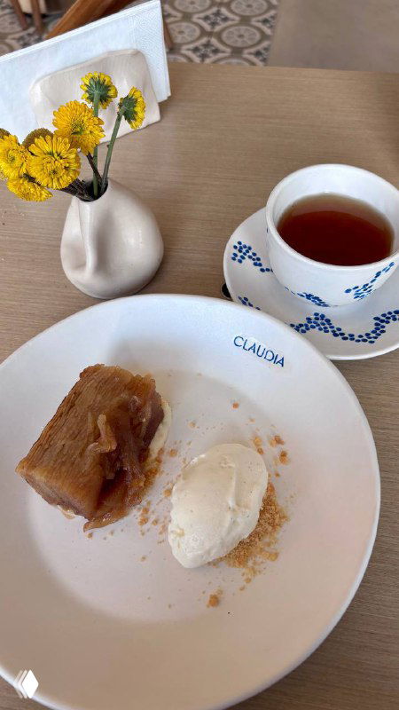Десертный кадр: яблочный татен с шариком мороженого на тарелке с логотипом Claudia и чашка чая, минималистичный столовый декор.