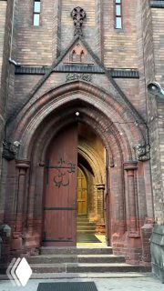 Главный вход в английскую церковь Святого Андрея: массивные деревянные двери с коваными элементами и арочный портал, открыт вечерний проход внутрь.