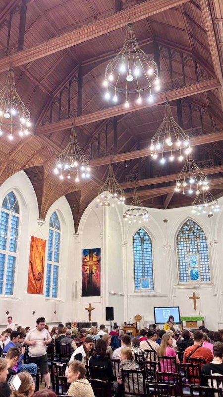 Внутренний простор англиканской церкви Святого Андрея во время службы: расставленные скамьи, деревянный сводчатый потолок и подвесные люстры.