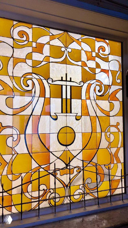 Витражная панель тёплых янтарных и охристых тонов с растительными мотивами и декоративной металлической решёткой в оконном проёме усадьбы.