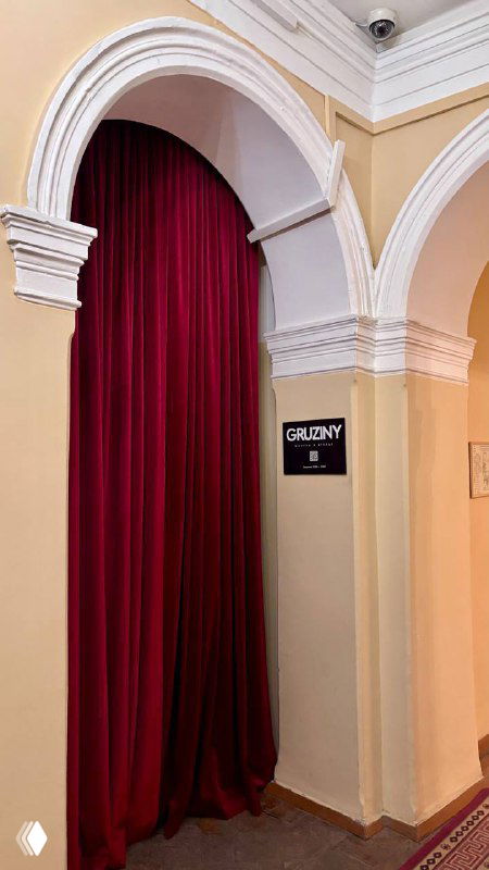 Арочный проём с высоким лепным потолком и тяжёлыми бархатными занавесями глубокого бордового цвета в одном из камерных залов усадьбы.