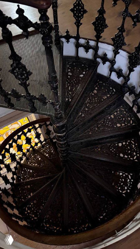 Вид сверху на винтовую лестницу: закрученные ступени чёрного чугуна, узорная кладка ступеней и симметричный центр лестничного пролёта в интерьере усадьбы.