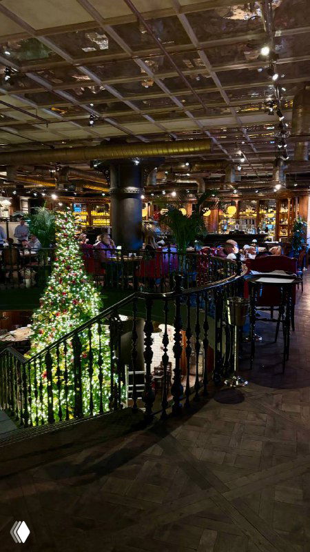 Интерьер ресторана: широкая винтовая лестница, украшенная рождественской ёлкой и праздничной иллюминацией, вид на зал и ограждение.