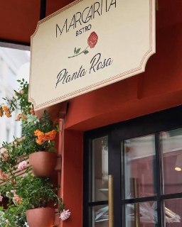 Фасад ресторана с вывеской Margarita Bistro, декоративные горшки с цветами и часть витрины — городская сцена заведения.