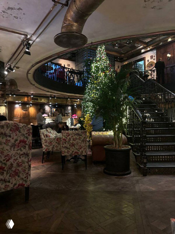 Просторный зал ресторана с витой лестницей, цветочными креслами и тёплой атмосферой; вид на верхний ярус и декоративные элементы.