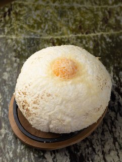 Десерт сферической формы, покрытый белой стружкой (возможно кокос), подан на темной подставке в эстетичной подаче ресторана