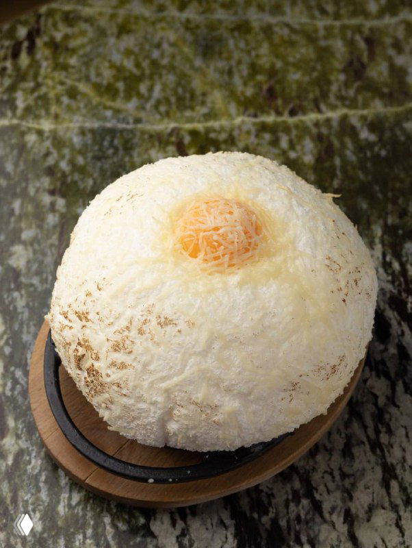 Десерт или хлебная подача: круглый тёплый шар с легкой посыпкой, сервированный на тарелке с деревянной подставкой — эстетичная подача блюда.