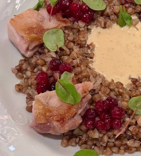Крупный план тарелки: гречка с кусочками перепелки, ягодами крыжовника и рядом сливочно-грибной соус, вид крупным планом.