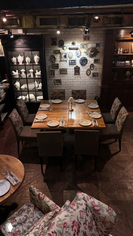 Набор столиков и полки с сервированными предметами: узорчатые кресла и тёплая деревянная отделка интерьера ресторана.