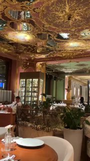 Большой зал ресторана с позолоченным потолком, зеркалами и столиками, вид на сервировку и общую атмосферу помещения.