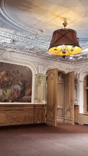 Интерьер с богатой лепниной на потолке, большой настенной живописной панелью, деревянными резными панелями и центральной люстрой.