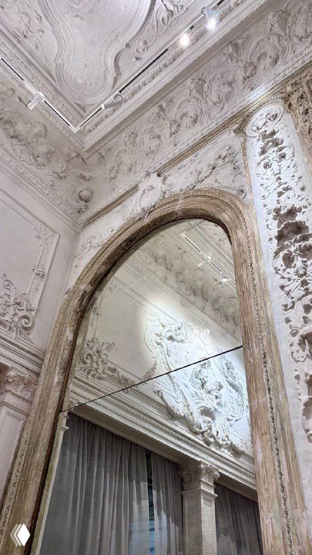 Отражение высокого арочного зеркала и лепных украшений на стене в одном из салонов усадьбы с богатой декоративной отделкой