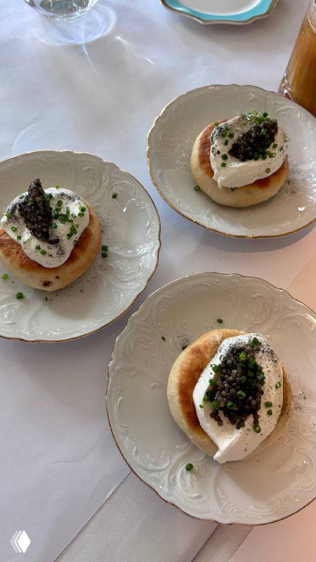 Тарелки с мини-беляшами, сверху — сметана и черная икра, крупный план сервировки на скатерти в бистро Le Pigeon.