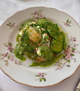 Порция с зелёным соусом, свежими огурцами и травами на фарфоровой тарелке с цветочным узором; крупный план, текстура соуса и гарнира.