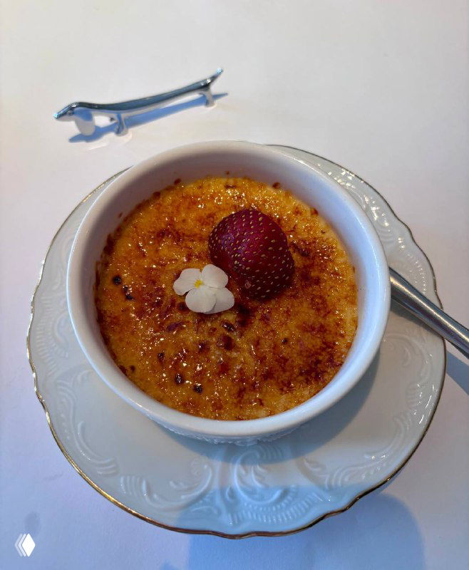 Крем‑брюле в керамической формочке с карамелизированной корочкой и ягодой сверху, сервировано на белой тарелке.