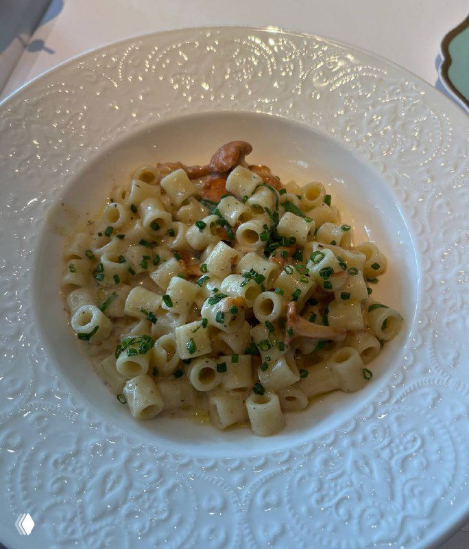 Паста с лисичками в кремовом соусе, сервированная в белой текстурной тарелке — крупный план пасты и грибов.