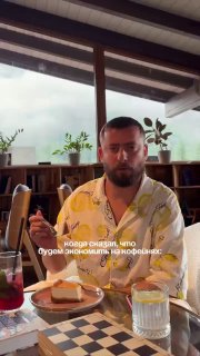 Кадр с мужчиной за столом, держащим прибор и кусочек еды; на столе тарелка и стакан, на фоне полка с растениями