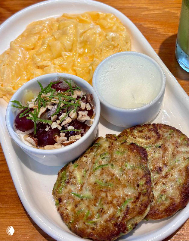 Порция завтрака в Flaner: скрембл, круглые драники и миска йогурта с маринованным виноградом, грецкими орехами и свежей мятой на деревянном столе.