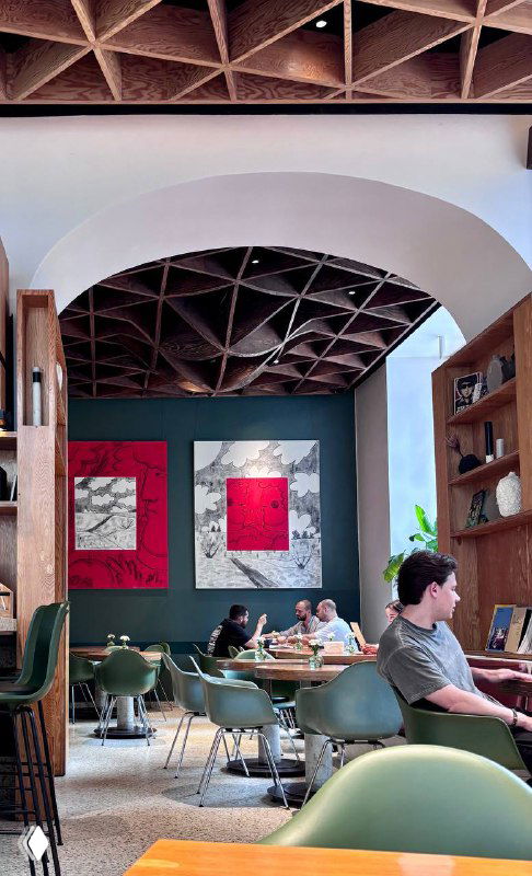 Глубокий вид на зал кафе с резным деревянным потолком, картинами на стене и сидящими посетителями — уютная атмосфера для завтрака.