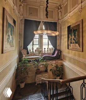 Интерьер лестничного холла в старом доме с уютным креслом у окна, антикварной мебелью и мягким светом из окна, камерная сцена.