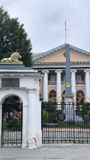 Фасад посольства с колоннами, двумя позолоченными львами у ограды и поднятым флагом над центральным входом.
