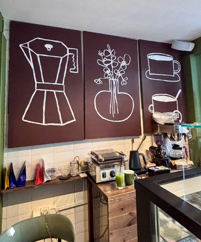 Интерьер кофейни «Короче кофе»: вид на барную стойку с кофейным оборудованием, панно с рисунками чашки и вазы и мелкие аксессуары.