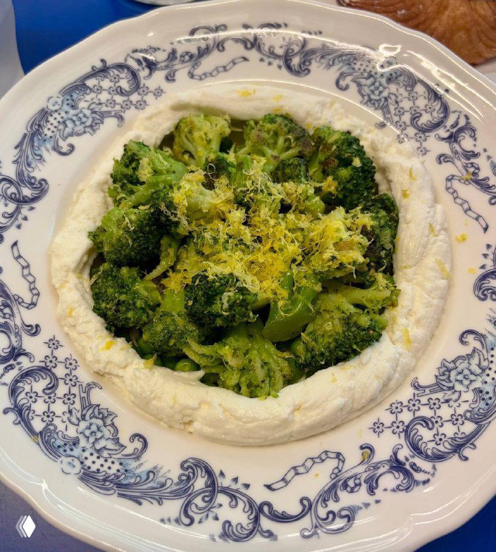 Тарелка брокколи со взбитой рикоттой, цедрой лимона и гороховой сальсой — сервировка на бело‑синем фарфоре в интерьере кафе Zoe.