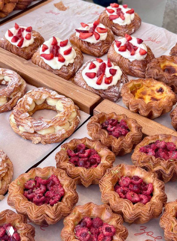 Витрина с выпечкой Zoe: даниши с кремом и клубникой, ромашковые пирожные и другие слойки, выложенные на деревянной подставке.